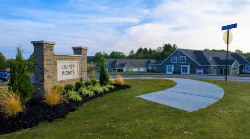 Entrance sign of Liberty Pointe Village community, featuring lush greenery and welcoming pathways.